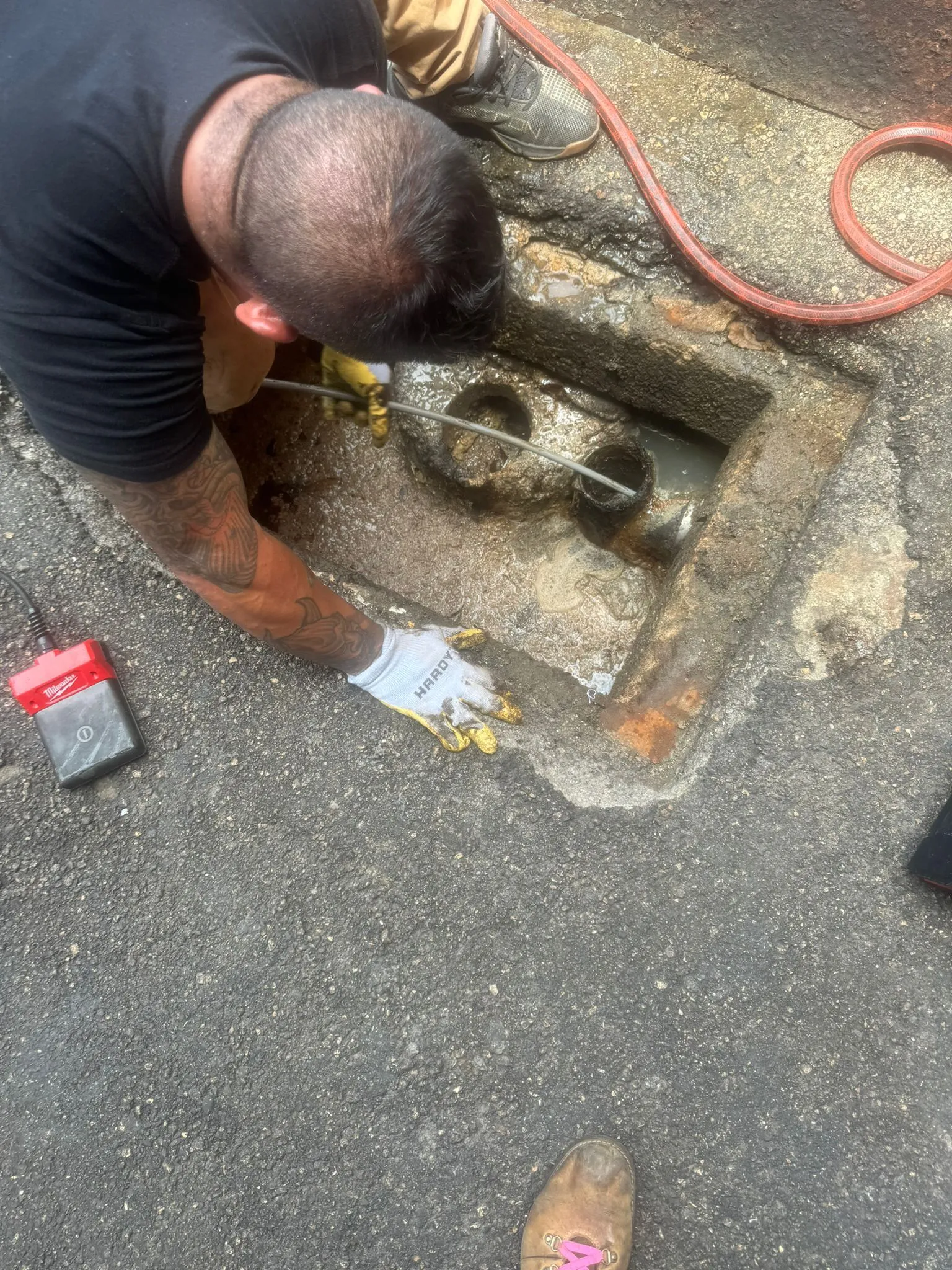 Plumber performs intensive underground drain cleaning work on an open pipe.