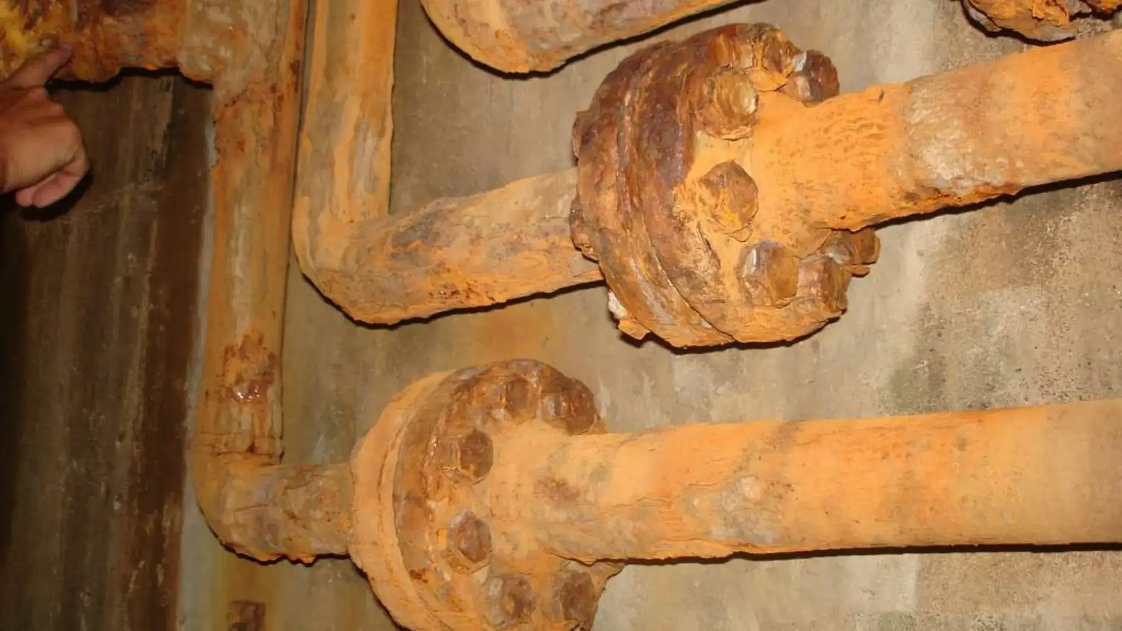 Close-up of severely rusted and corroded cast iron pipes, showing large flanges bolted together.