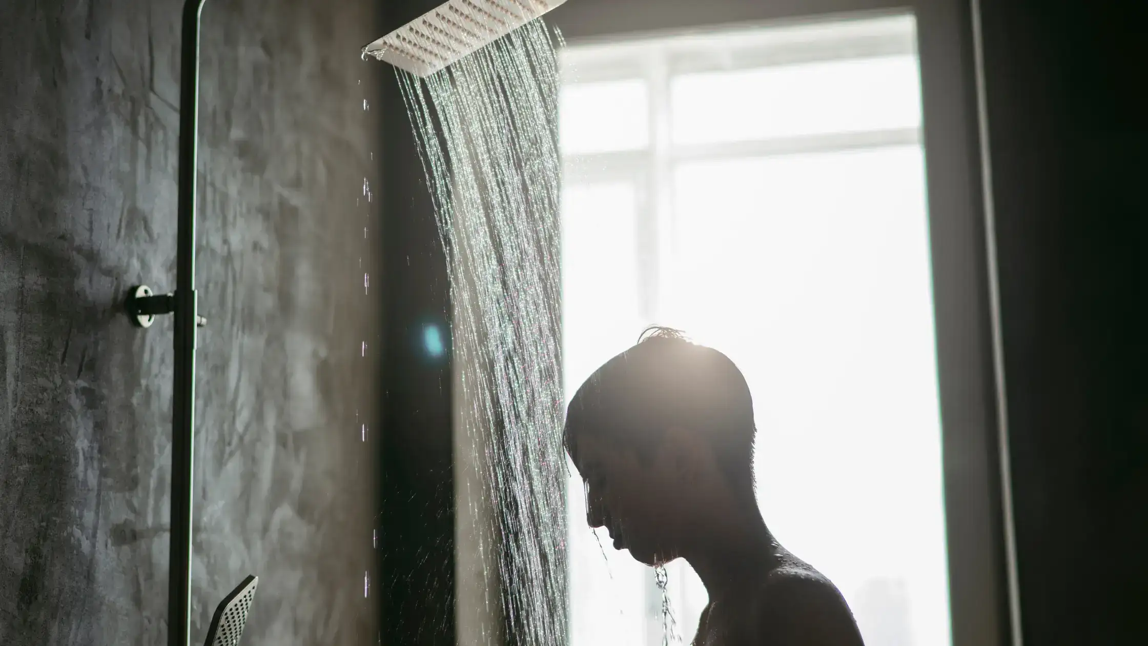 
A silhouetted boy stands under a shower with a Weak Hot Water Pressure. 
