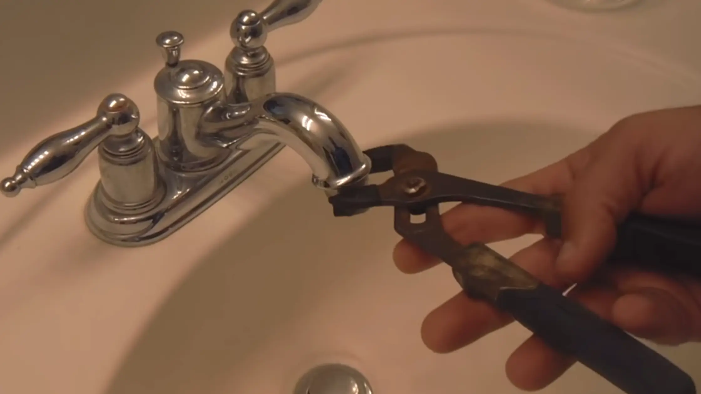  A hand uses pliers to work on a chrome bathroom faucet that has low shower pressure.