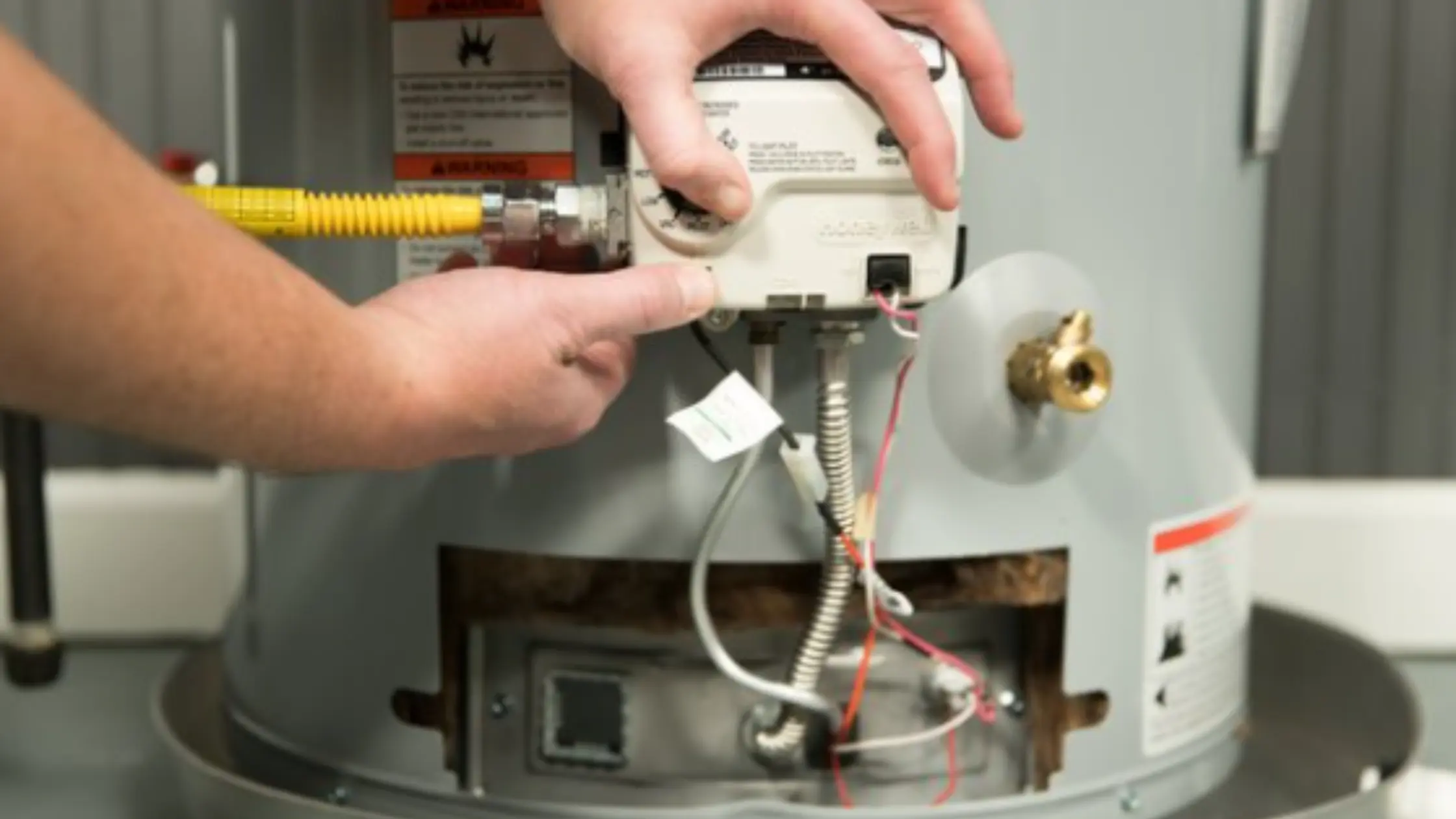 
Close-up of a hand adjusting the control valve on a water heater, indicating issues with Aging Ignition Components.